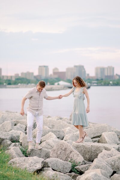 man holding his fiance's hand as she walks on rocks