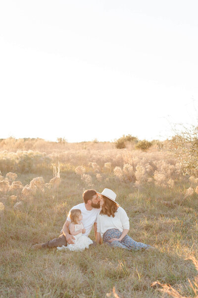 Sweetest Orlando family kissing in a field of tall pampas grass at sunset during their photo session