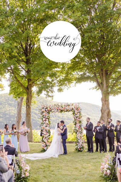 Bride and groom kissing during their outdoor ceremony in front of a spring floral arch  at  Monteverde at Oldstone