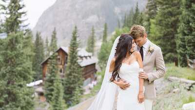 Bride and groom posing outside surrounded by trees and mountains