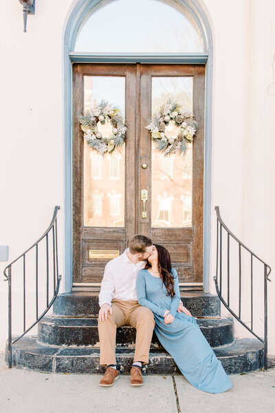 Dusty blue styled engagement session kissing on steps of historic downtown building