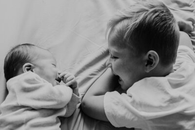 Een gezin ligt samen op bed met hun pasgeboren baby, omringd door kussens en dekens, stralend van blijdschap.
