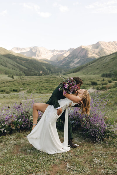 groom dipping bride back while kissing her with mountains in the background