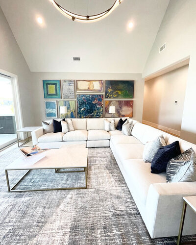 A living room designed by a Frisco interior designer, featuring an elegant fabric white couch, colorful artwork as a pop of color, and blue accessories for a sophisticated touch.