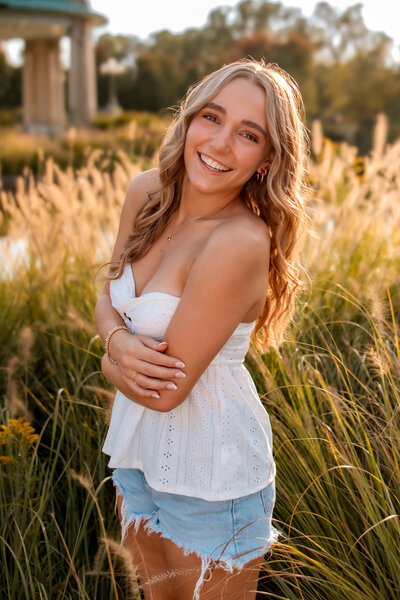 a blonde haired girl in a tight white dress  standing by a cement railing  next to a lake at  The Grand Basin in Forest Park at sunset.