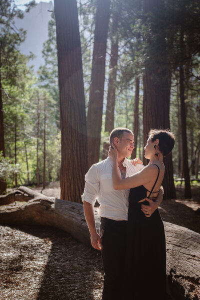 A couple hugs and smiles at each other in a forest in Yosemite