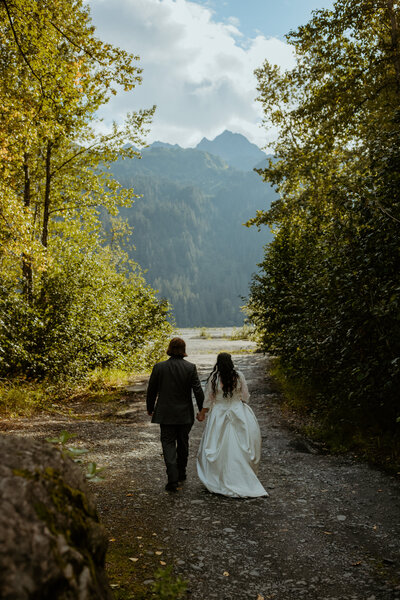 bride and groom walk away from the camera towards a lake