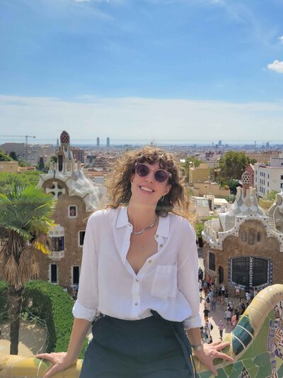 Award-winning luxury travel expert Stephanie Dosch at Park Güell in Barcelona, Spain, leaning on a colorful mosaic railing with Gaudí-designed buildings and a city skyline in the background ©Stephanie Dosch | theViatrix Luxury Travel