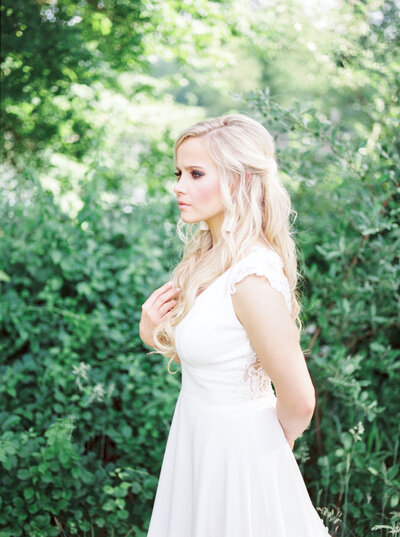 Blonde bride looking to the left in front of green bushes