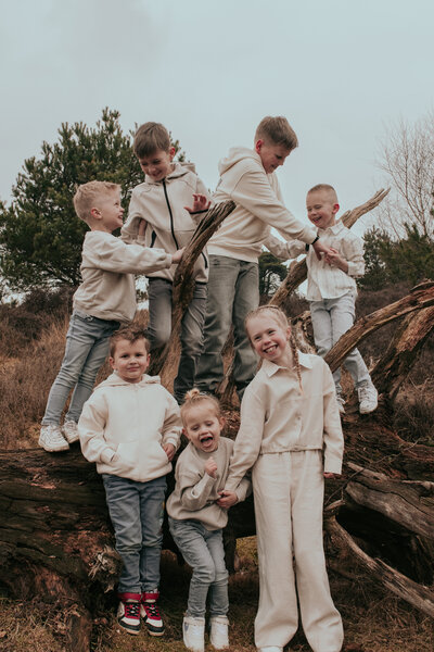 Een groep kinderen staat op een boomstam in de natuur, lachend en samen spelend.