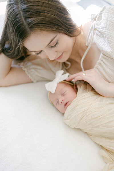 women laying down with swaddled baby on bed smiling knoxville tennessee newborn photographer