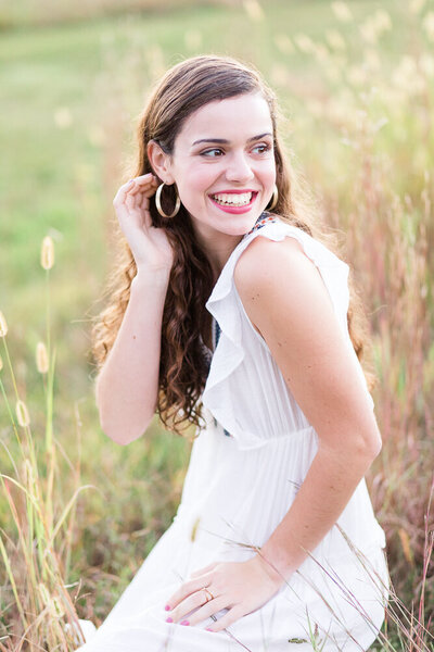 High school senior girl wearing a white flowy dress at a field during golden hour photo  session.