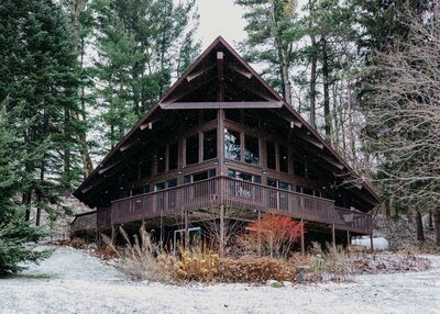 A small photo of a couple standing in a field surrounded by trees. They are facing each other, embracing with foreheads touching as they smile for the photo.