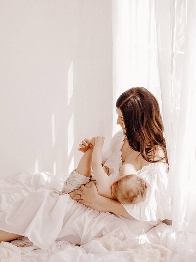 breastfeading mother sitting on bed in a white dress