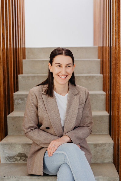 Nutritionist sitting on stairs inside with brown jacket