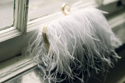 A white feather clutch purse sitting up against a window sill.