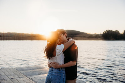 Engaged couple share a sunset kiss during their engagement photography session on the shores of Lake Burley Griffin, Canberra ACT. By Acacia & Grace Photography