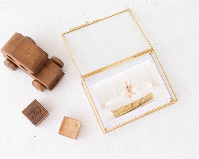 detail shot of gold glass photo box with a photo of a baby sitting in a Moses basket.