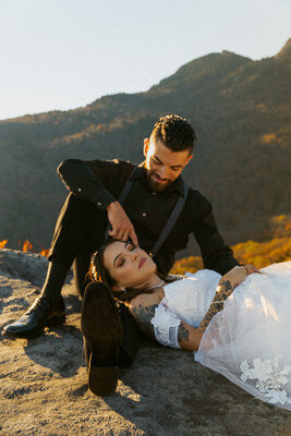 couple in elopement attire sitting on a rock. bride laying in grooms lap