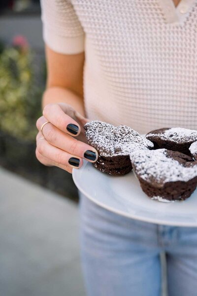 Woman with black fingernails holding a plate with chocolate mini cakes.