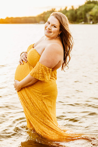 pregnant mom in yellow dress playing in the lake at sunset near Green Bay