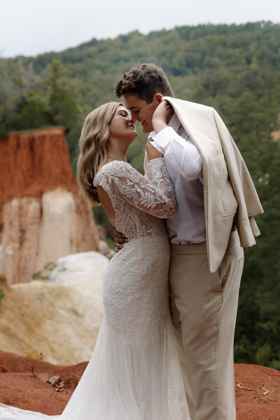 Candid elopement moment as couple leans in for a kiss, groom holding his tan suit, surrounded by red rock cliffs.