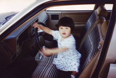 Susan Ly as a baby driving an old car