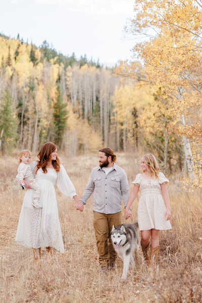 A happy couple holds hands with their teen daughter while walking a Frisco Peak trail with their husky and baby on mom's hip