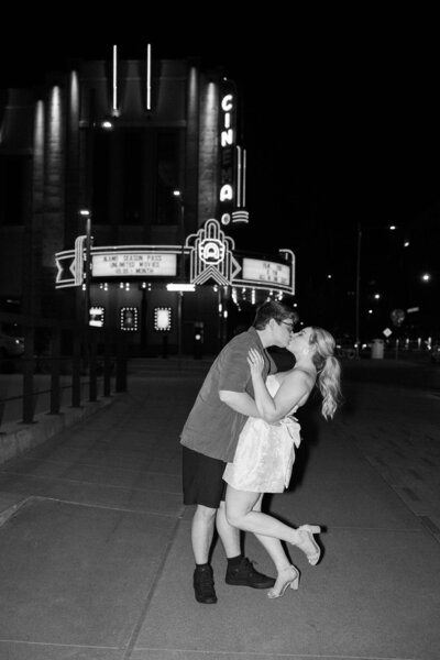 Denver Engagement Photographer, Engaged couple kisses in front of illuminated theater during portrait session.