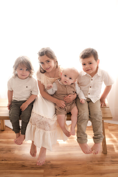 Four siblings sitting together on a bench in Hope's in home Carson City studio.