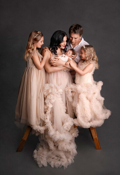Beautiful mom and daughters in cream ruffle gowns holding her newborn boy with their dad  at their motherhood studio session in Toronto area.