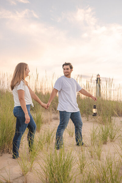 couple stands on the beach outside of the cape henry lighthouse