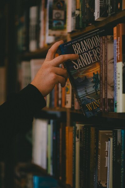 Hand pulling out Wind & Truth by Brandon Sanderson from a bookshelf