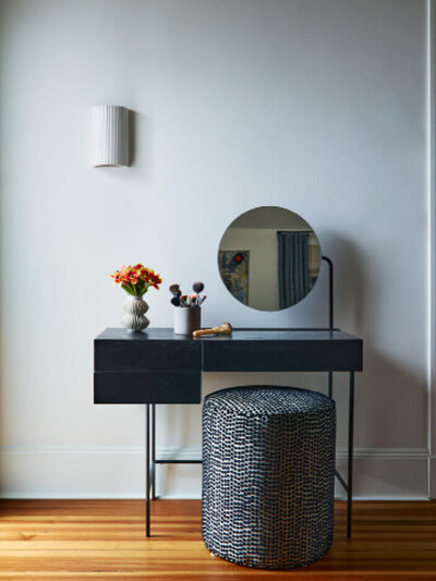 Interior decorators in Boston designed a minimalist makeup vanity with modern furniture and a custom Pierre Frey pouf at a Brookline home renovation project.