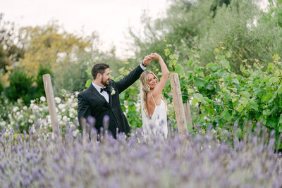 groom in a traditional black tux twirling his bride in the lavender field at Tuscan Rose Ranch during golden hour captured by Los Angeles Wedding Photographer Magnolia West Photography