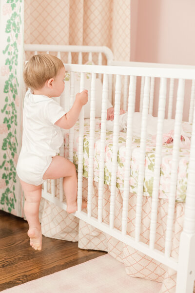 Toddler climbing into crib to see his baby sister - Newborn Photographer Greenville