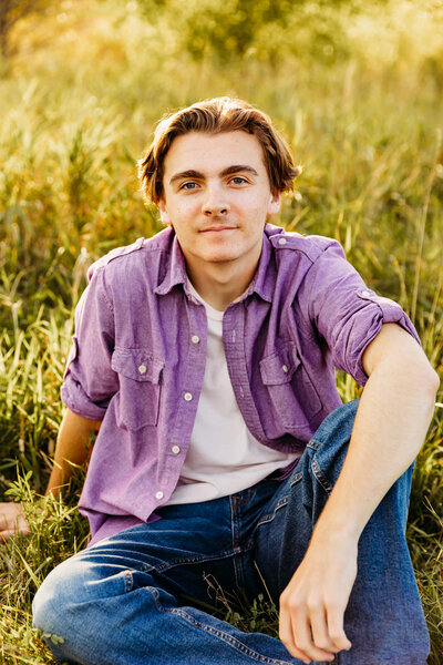 teenage boy sitting in a grassy field for his green bay senior photo session
