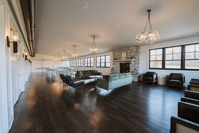 Lounge with globe lights, brick fireplace, green velvet couches, and dark hardwood floors