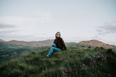 woman is sat on a green meadow atop a mountain in snowdonia
