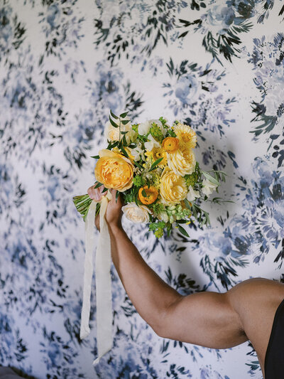 muscled arm holding a yellow flower bouquet in front of a blue flower wallpaper
