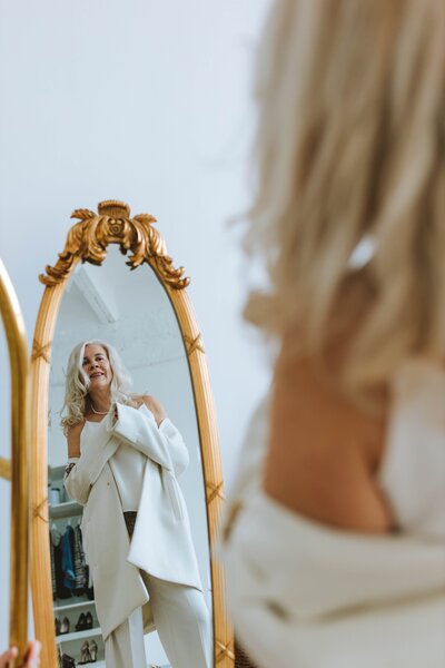 The woman beams with delight as she observes her reflection in the mirror, radiating joy and self-appreciation