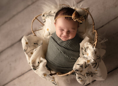 smiling baby wrapped in green waffle knit in a wire basket