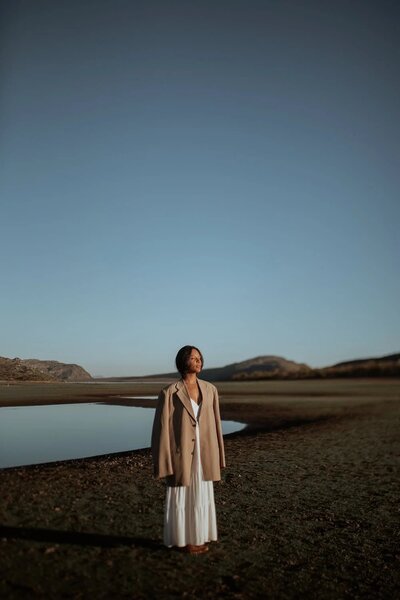 A contemplative figure stands against a serene lakeside backdrop