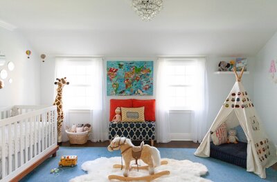 A fun and whimsical neutral children's nursery featuring a tent, rocking horse, large stuffed giraffe, and colorful accents. colorful accessories