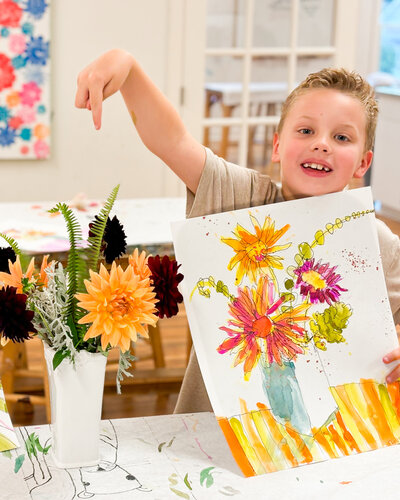 Boy showing his floral painting next to a still life of a flower bouquet