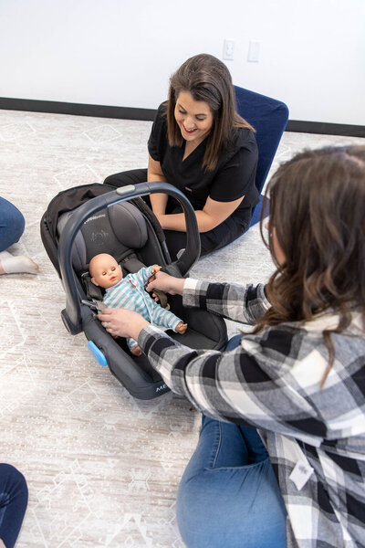Women learning how to use car seats with dolls