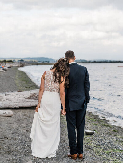 a bride and groom walk hand-in-hand along the beach on Camano Island photographed by Pacific Northwest elopement photographer Amy Galbraith