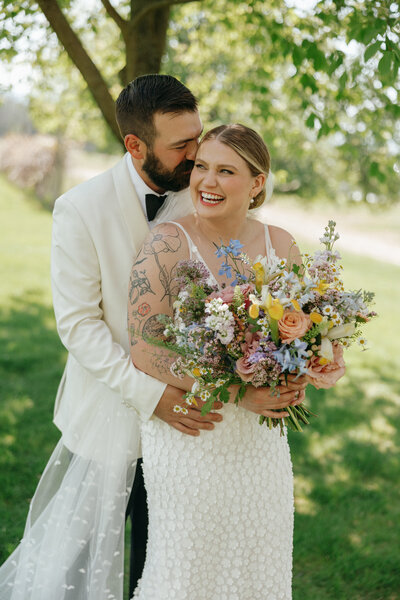 Groom embracing bride holding colorful floral bouquet