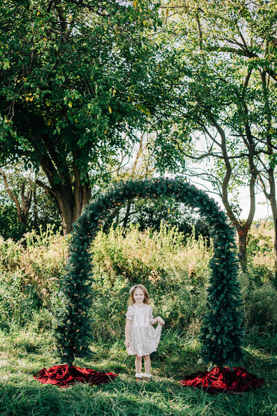 the holiday arch mini session in rio, wi with a young girl wearing a champagne colored sequin dress while posing. 