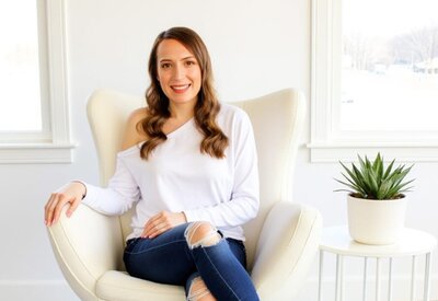 Stacey from Xanthe Bookkeeping smiling in a white sweatshirt while seated in a modern white egg chair, shown in the website footer bio section.